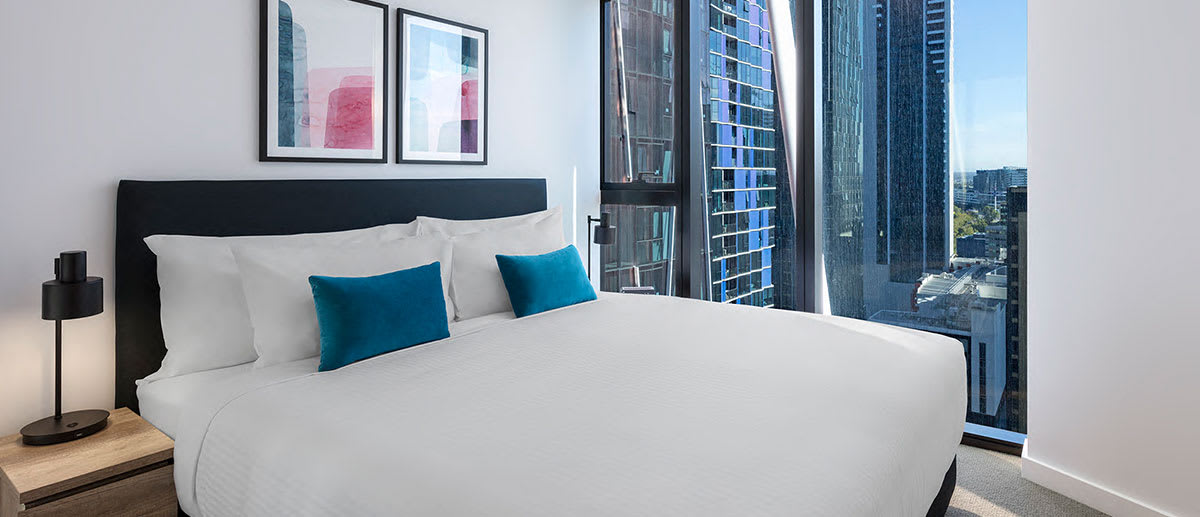 Big queen size bed in 1 Bedroom Apartment in Central Melbourne hotel with large windows and views of city outside