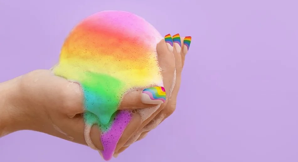 An illustration of a hand with rainbow-coloured fingernails, holding a rainbow-coloured sphere, dripping rainbow paint.