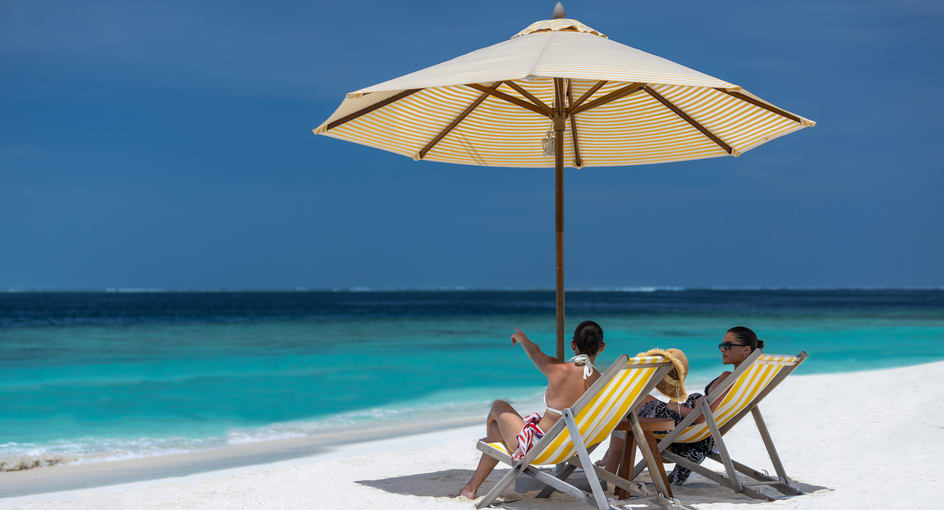 Guests sitting and relaxing on the sandy beach of Avani+ Fares Maldives Resort