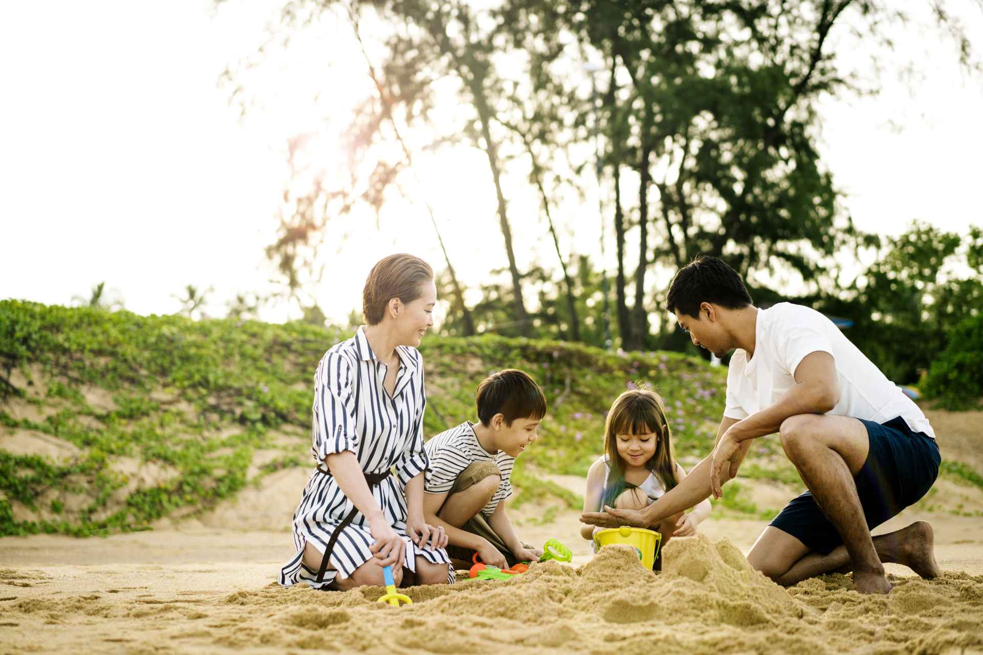 A family of four (father, mother, son, daughter) building sand castles on the beach.