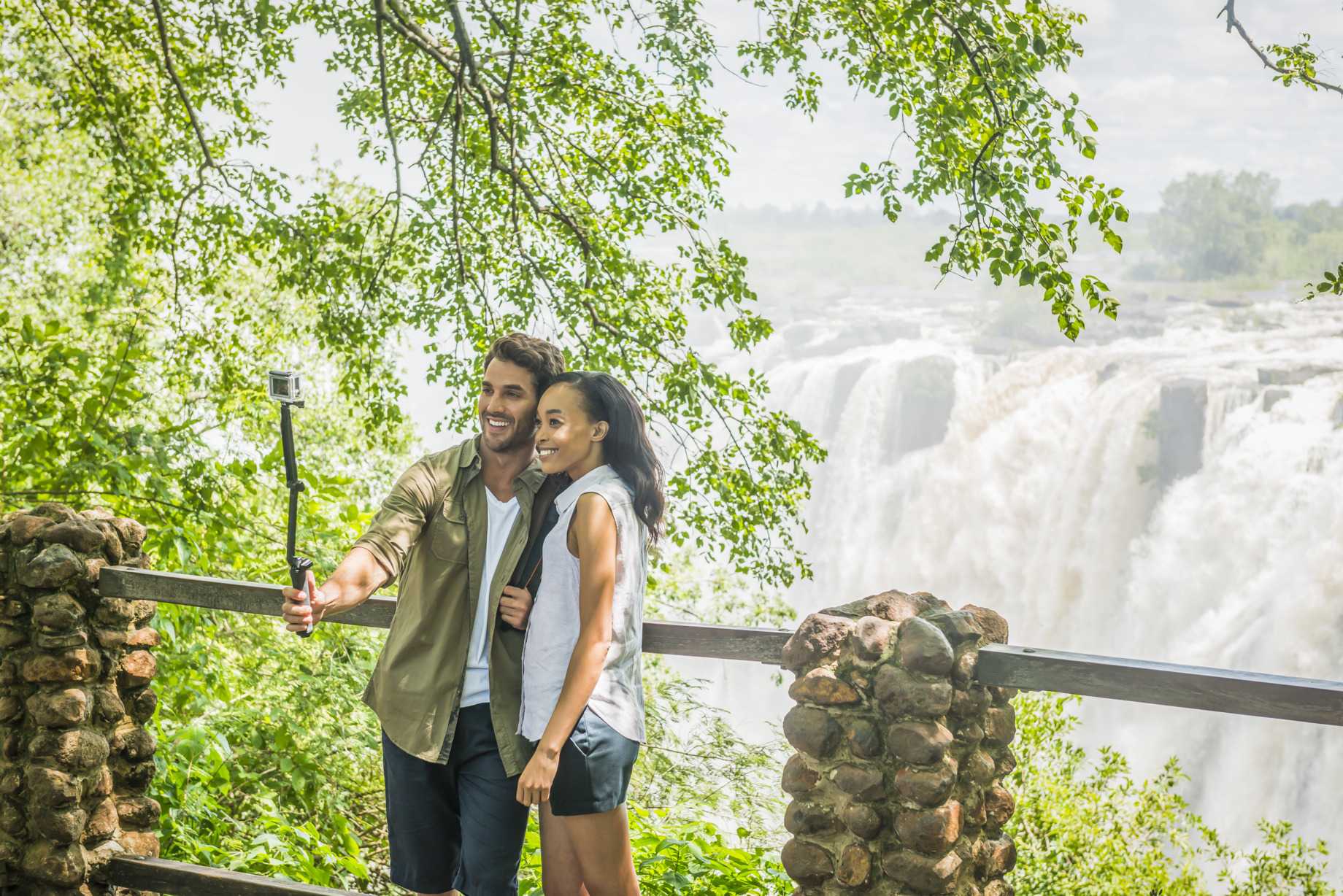 A couple with a selfie stick taking photos in front of the Victoria Falls.