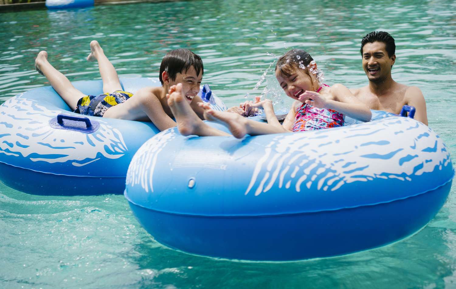 Two children (on two pool floats) and an adult having fun in the swimming pool.