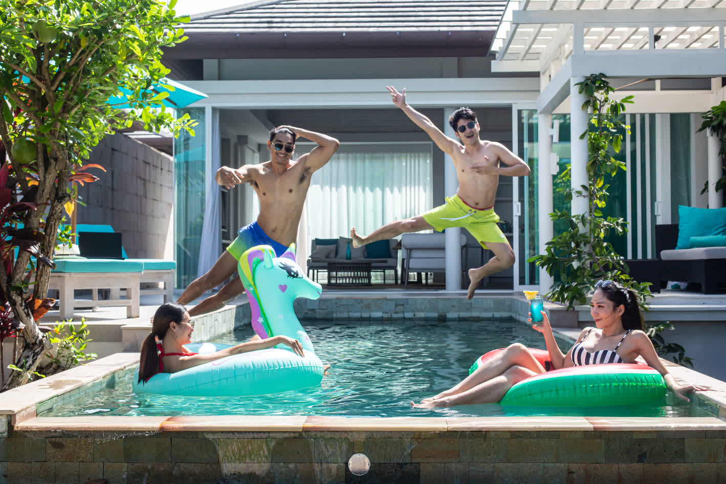 Four adults having fun in the swimming pool (two adult men are jumping in the air into the pool).