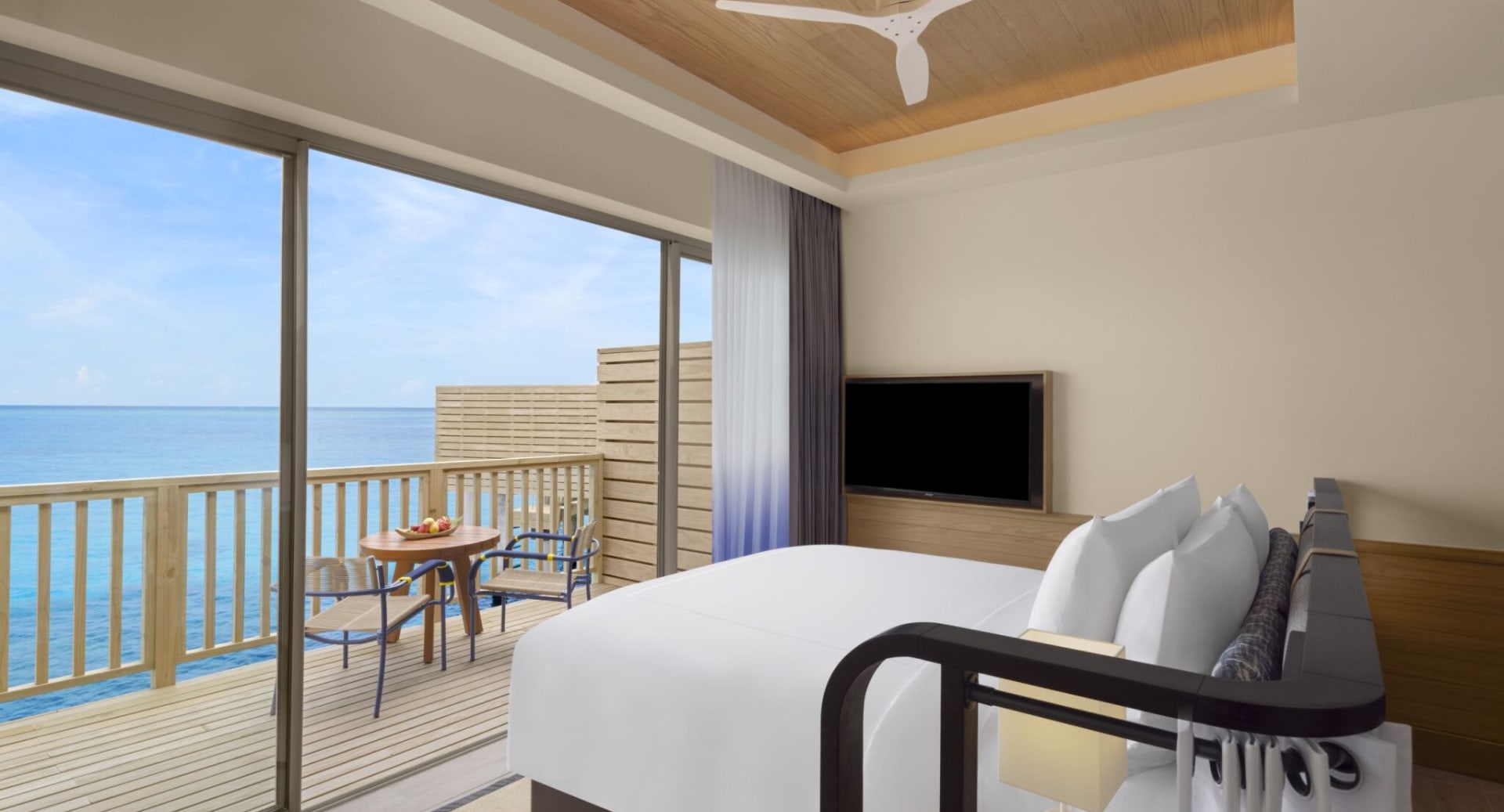 Overwater villa bedroom with balcony and ocean view at Avani+ Fares Maldives.
