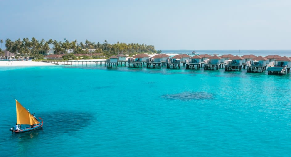 Aerial view of the Ambaa cocktail boat floating towards the over water villas at Avani+ Fares Maldives Resort