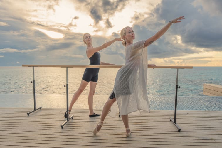 Two women, Gemma Louise Deeks on the left and Karis Scarlette on the right, striking a ballet pose infront of the ocean at Avani+ Fares Maldives Resort.