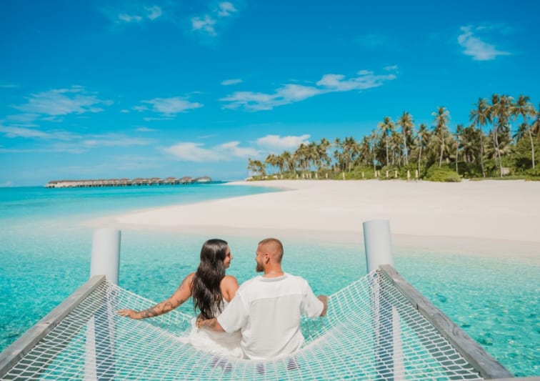 Couple sitting on an overwater hammock at Avani+ Fares Maldives Resort