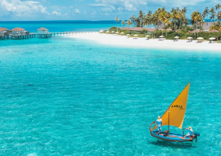 Aerial view of the Ambaa cocktail boat floating towards the over water villas at Avani+ Fares Maldives Resort