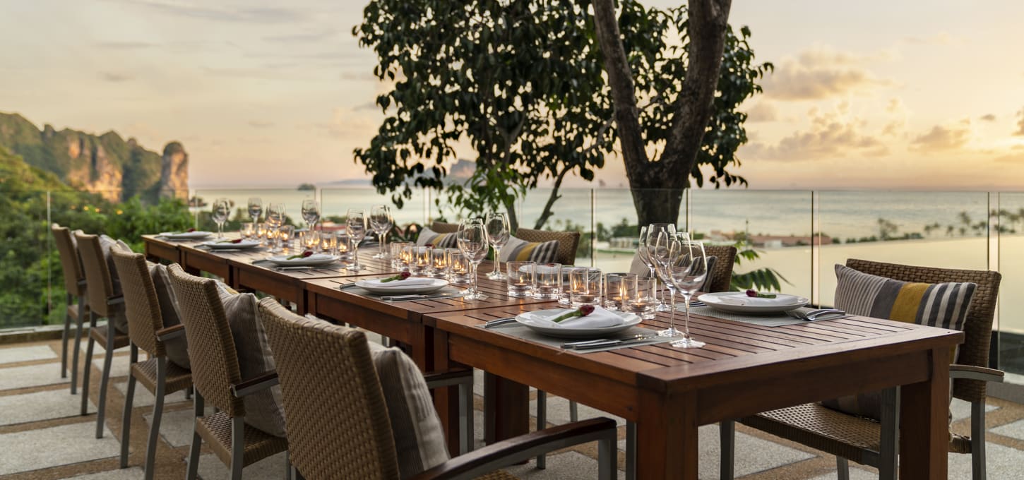 Exterior view of outdoor table setup at Orchid Bar with view of Infinity Pool and ocean at sunset