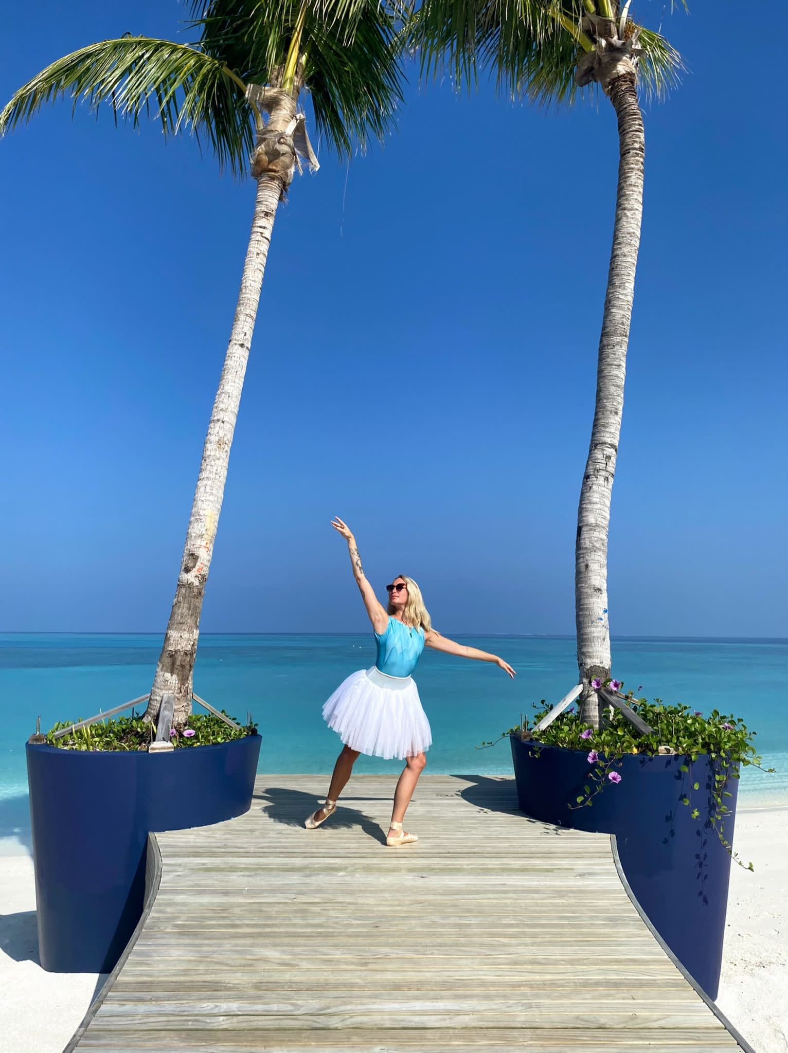 Karis Scarlette in a ballet pose between two trees, in front of the ocean at Avani+ Fares Maldives Resort.