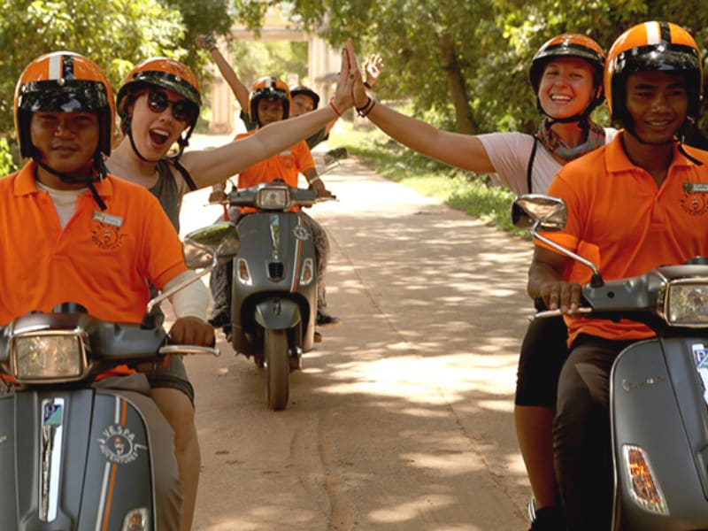 Tourists riding at the back of a Vespa motorcycle in Siem Reap