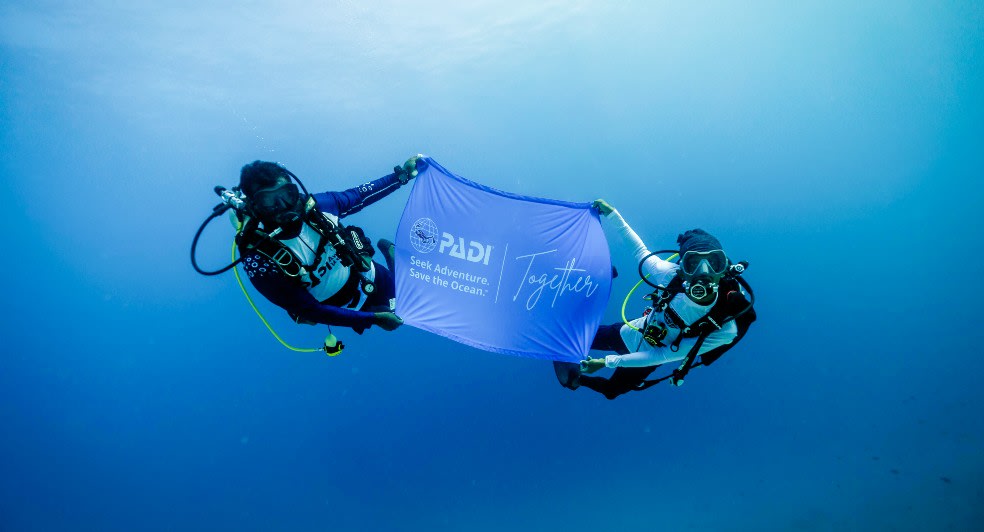 PADI Aware Week 2025 held at Avani+ Fares Maldives Resort - Divers with event banner underwater