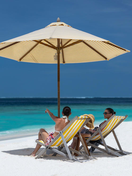 Guests sitting and relaxing on the sandy beach of Avani+ Fares Maldives Resort