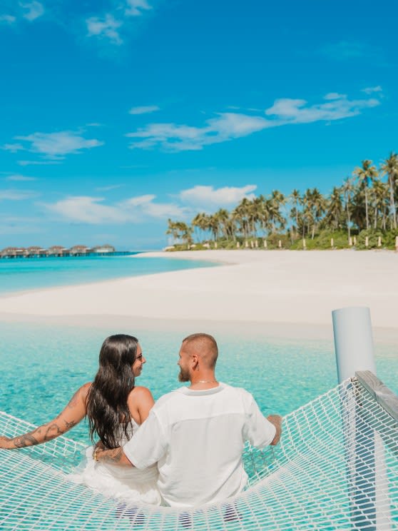 Couple sitting on a overwater hammock at Avani+ Fares Maldives Resort