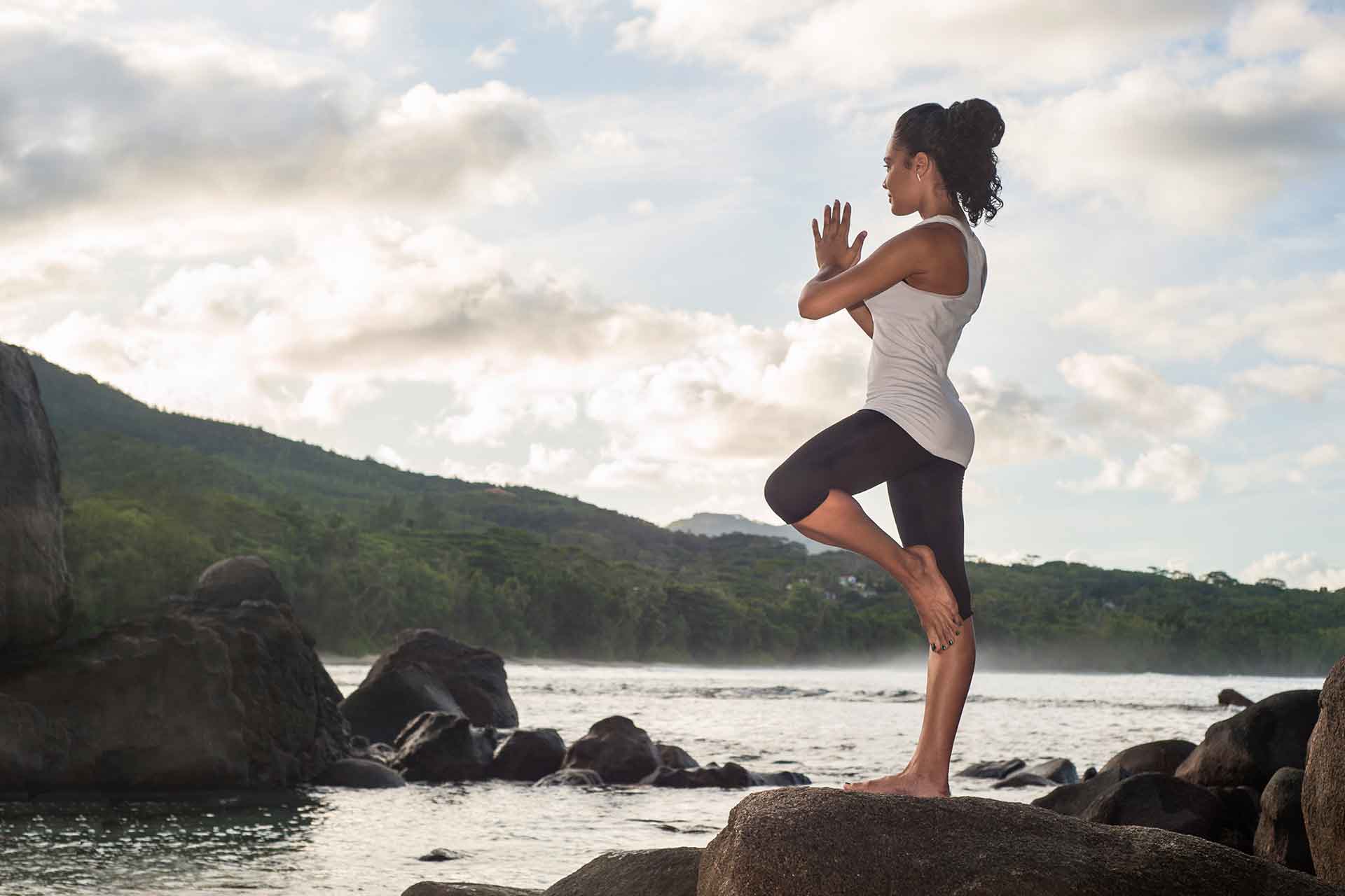 A girl doing yoga on a cliff of Seychelles